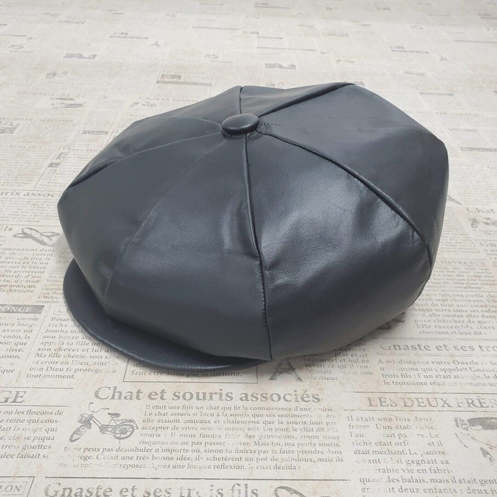 A black leather hat sitting on top of a newspaper.