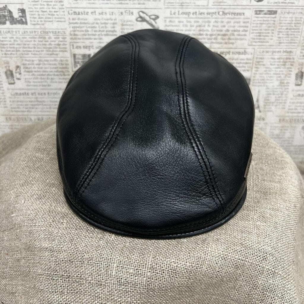 A black leather hat sitting on top of a tan blanket.