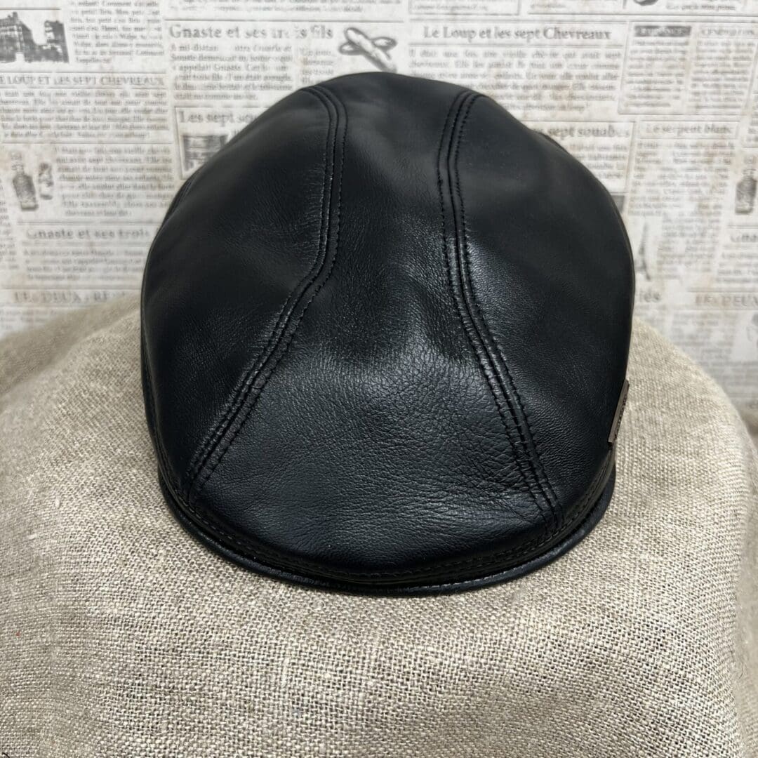 A black leather hat sitting on top of a tan blanket.