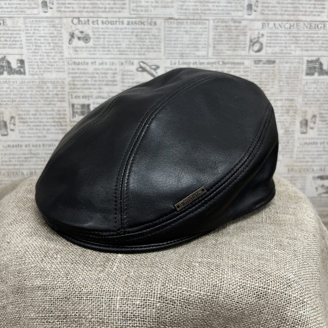 A black leather hat sitting on top of a tan blanket.