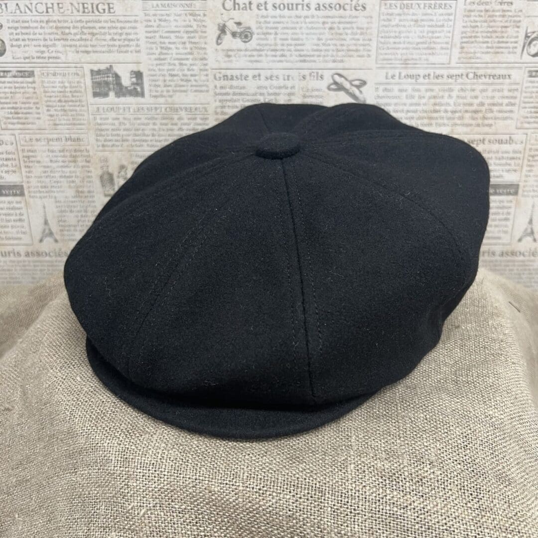 A black hat is sitting on top of a tan blanket.