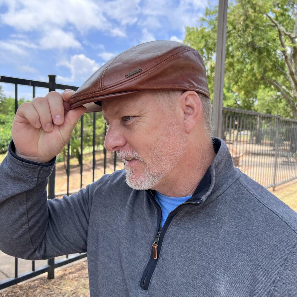 A man in grey jacket holding his hat up to the side of his head.