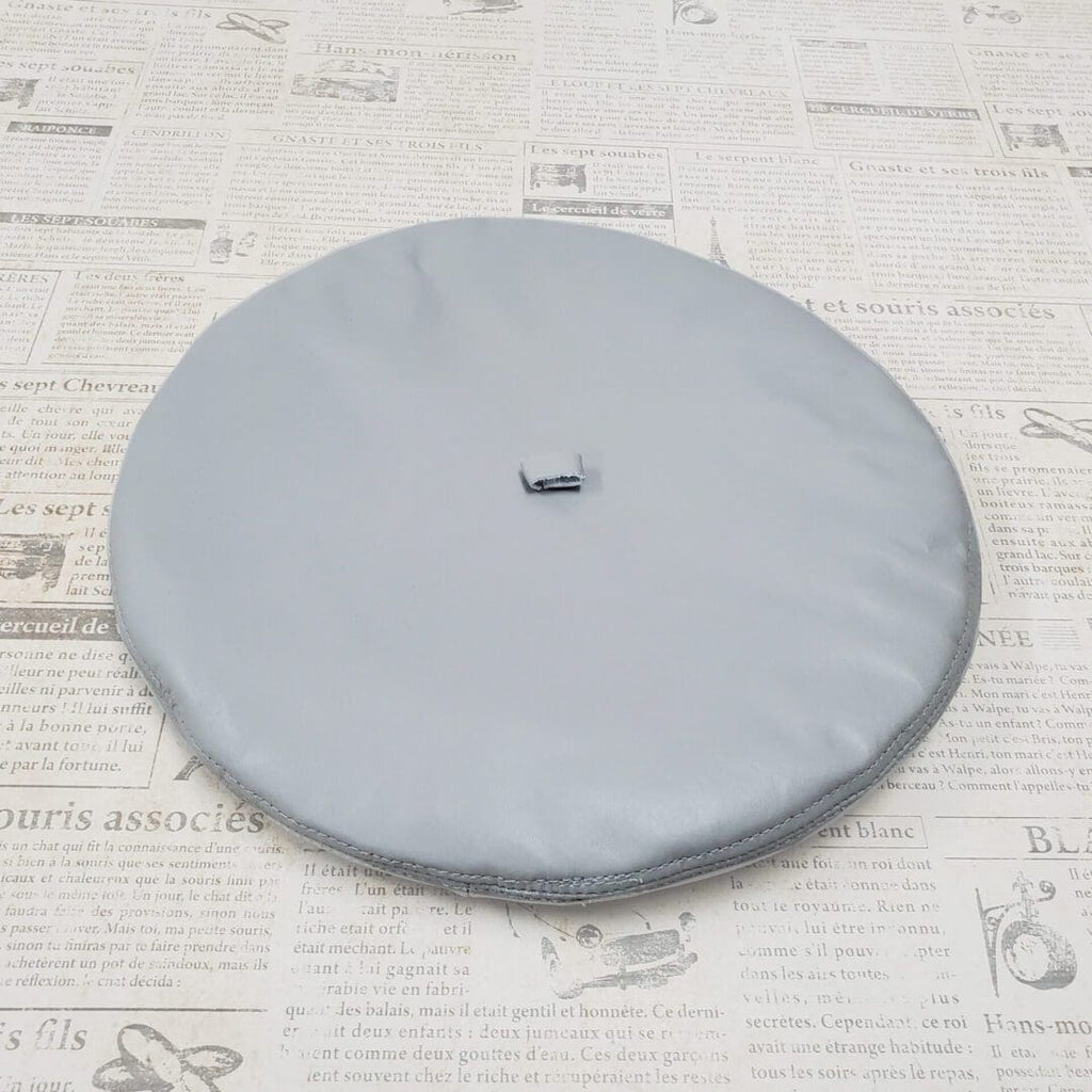 A round gray pillow sitting on top of a white sheet.