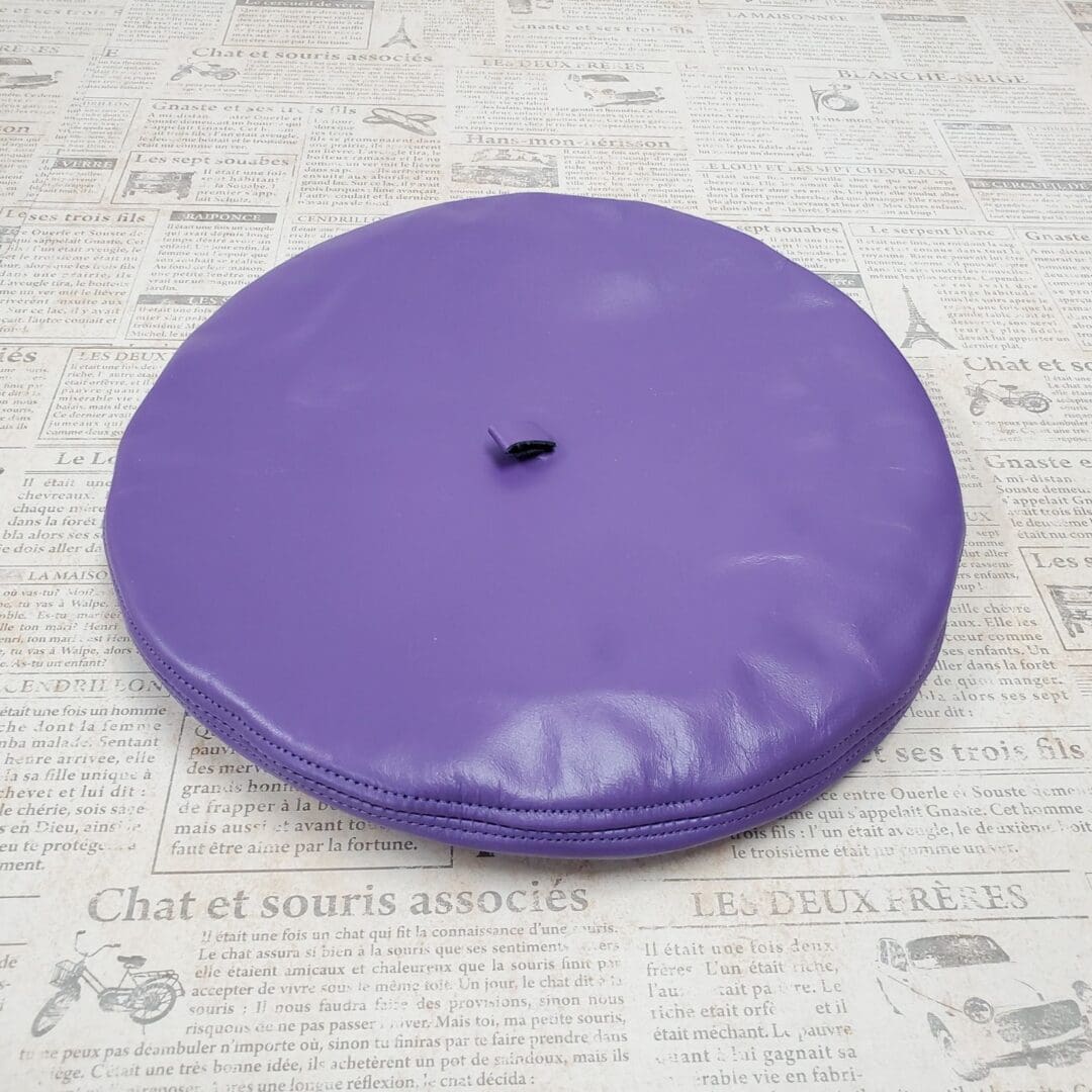 A purple round pillow sitting on top of newspaper.