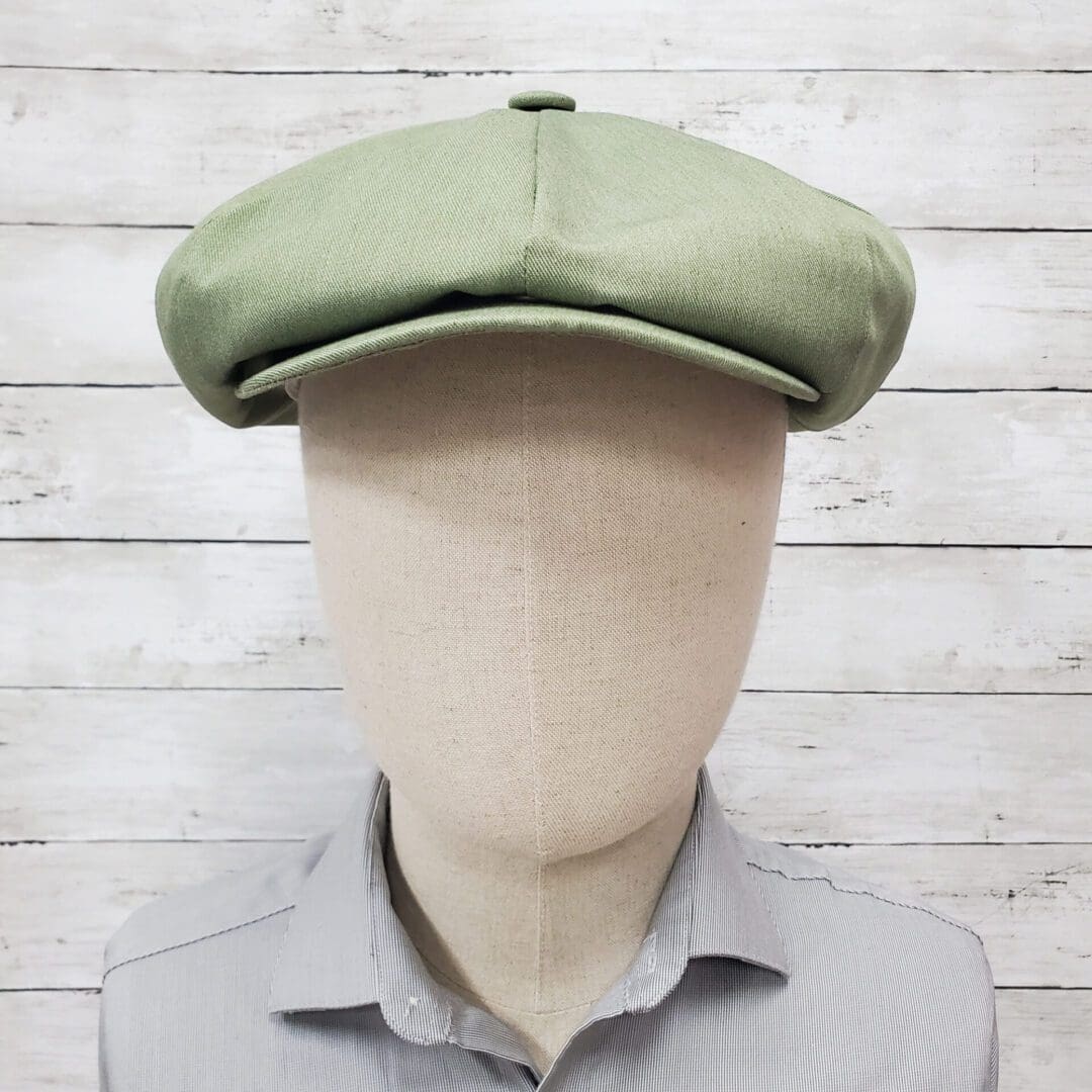 A man with a green hat is standing in front of a white wall.